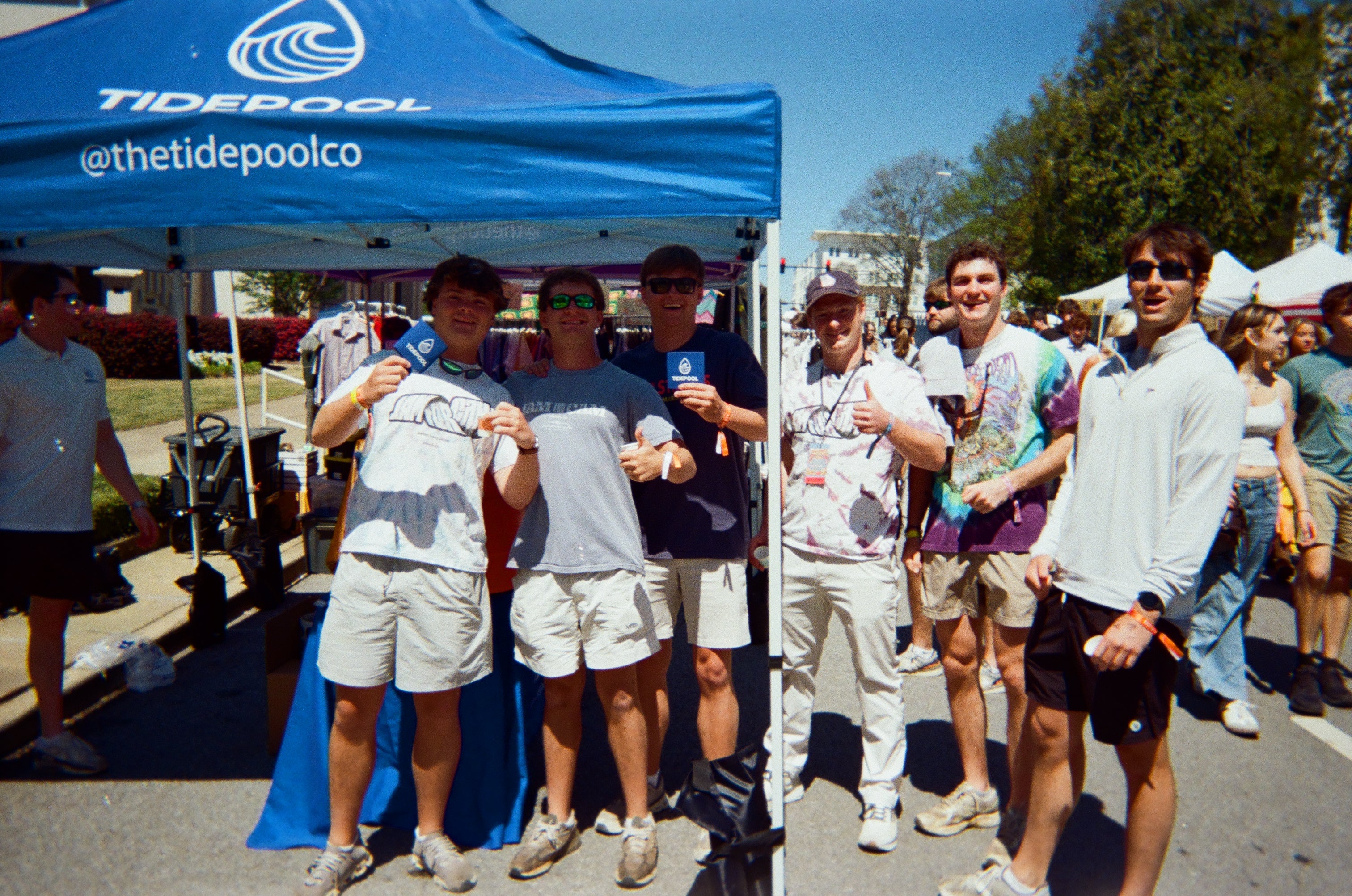 Group of people under a blue tent with 'Tidepool' branding, holding items.
