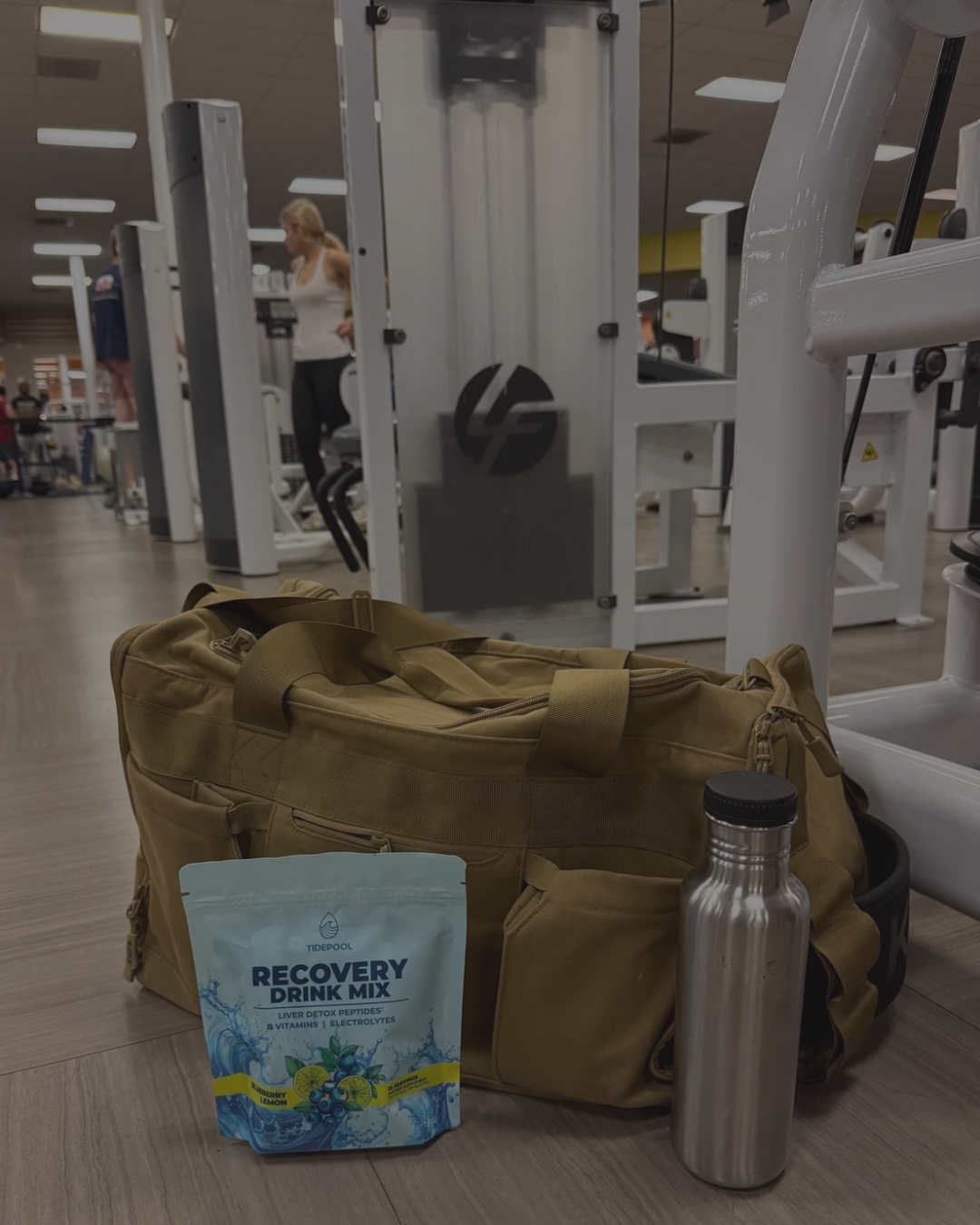 Brown duffel bag with recovery drink mix packet and water bottle on gym floor