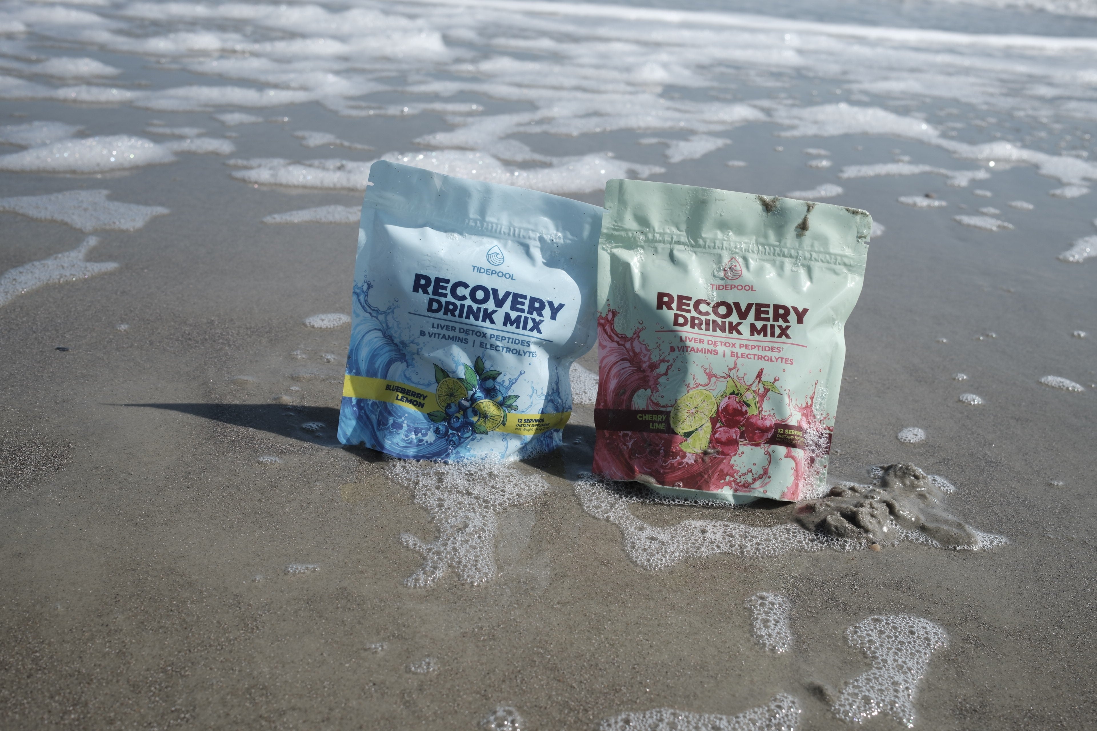 Two packages of recovery drink mix on a sandy beach.